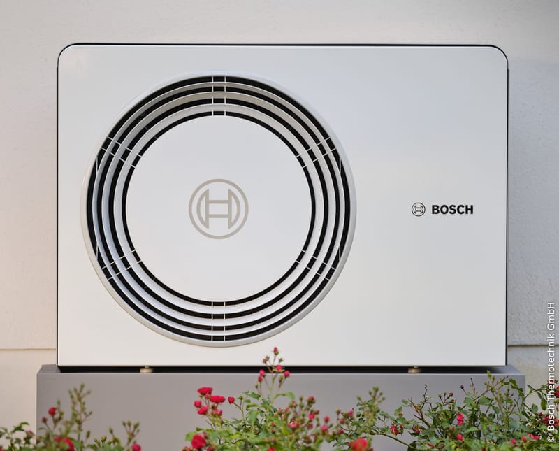 Bosch-Außeneinheit Compress AW OR der Compress 5800i AW und 6800i AW vor einer hellen Hauswand